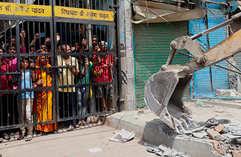 Des habitants se tiennent derrière un portail en fer alors qu'un bulldozer démolit une structure à Jahangirpuri, Delhi, Inde, le 20 avril 2022.