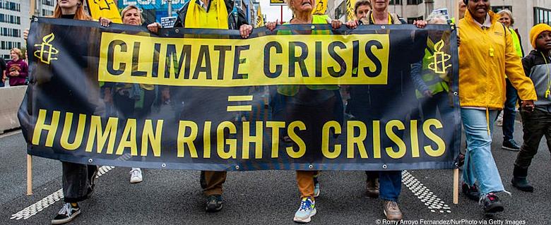 des manifestants défilent et portent une banderole signifiant : "la crise climatique = une crise des droits humains"