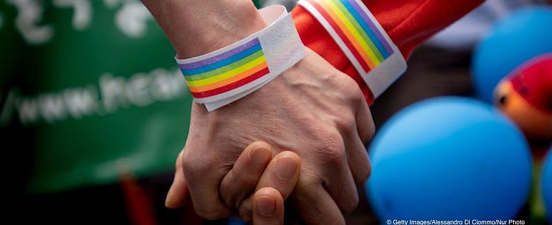 deux mains se tiennent, avec autour des poignets, un bracelet aux couleurs arc en ciel